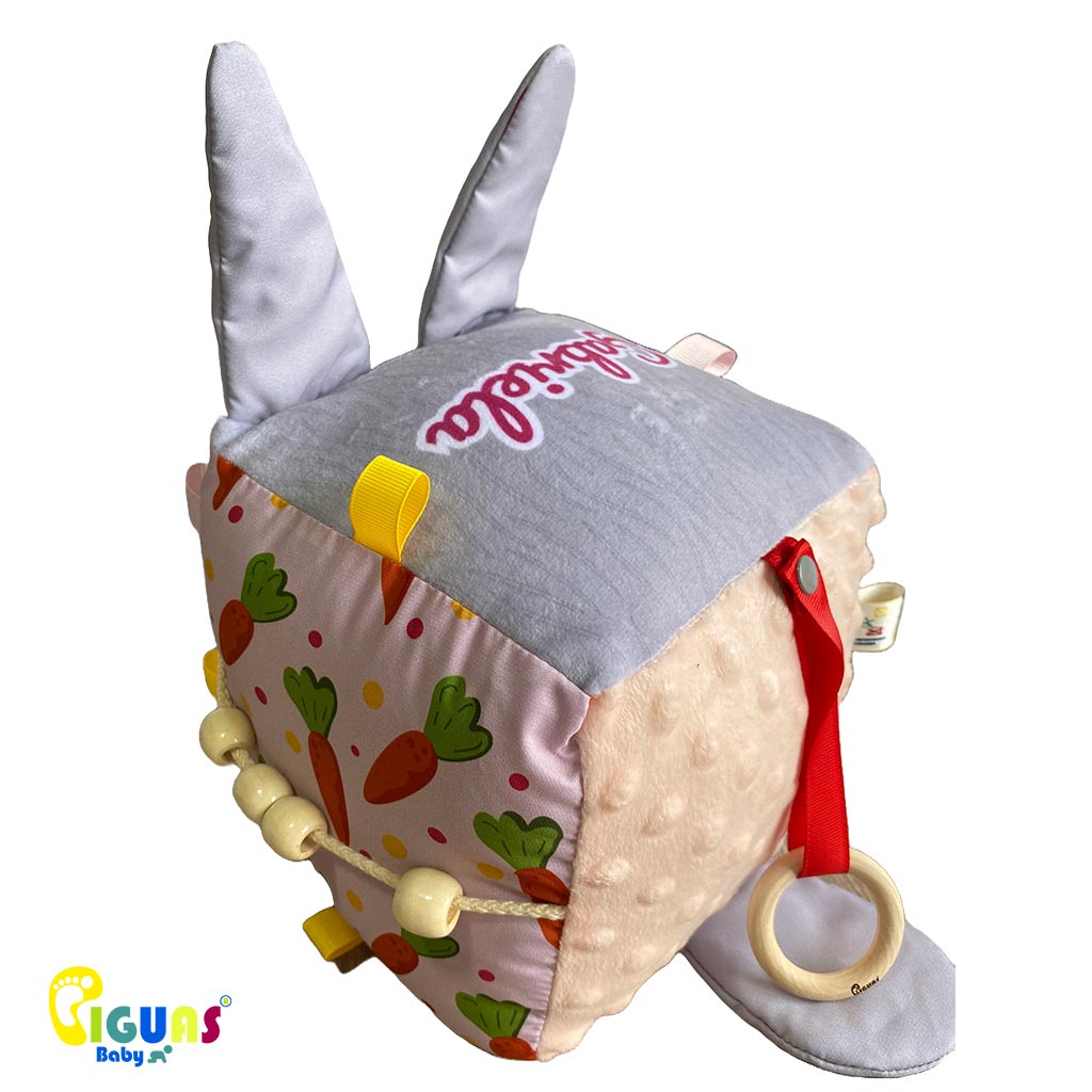 Cubo sensorial con forma cara del conejo mas inteligente que emite sonidos al agitarlo, al ser sonajero, y al agarrar sus orejas, al estar hechas con papel crujiente, ideal para el desarrollo auditivo del bebé.