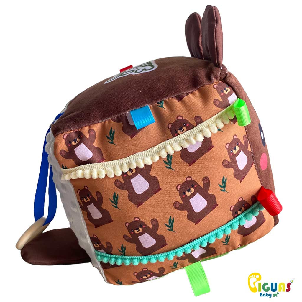 Un cubo sensorial para bebés con la cara de un osito aventurero, perfecto para estimular la vista, la audición y el tacto de tu bebé.