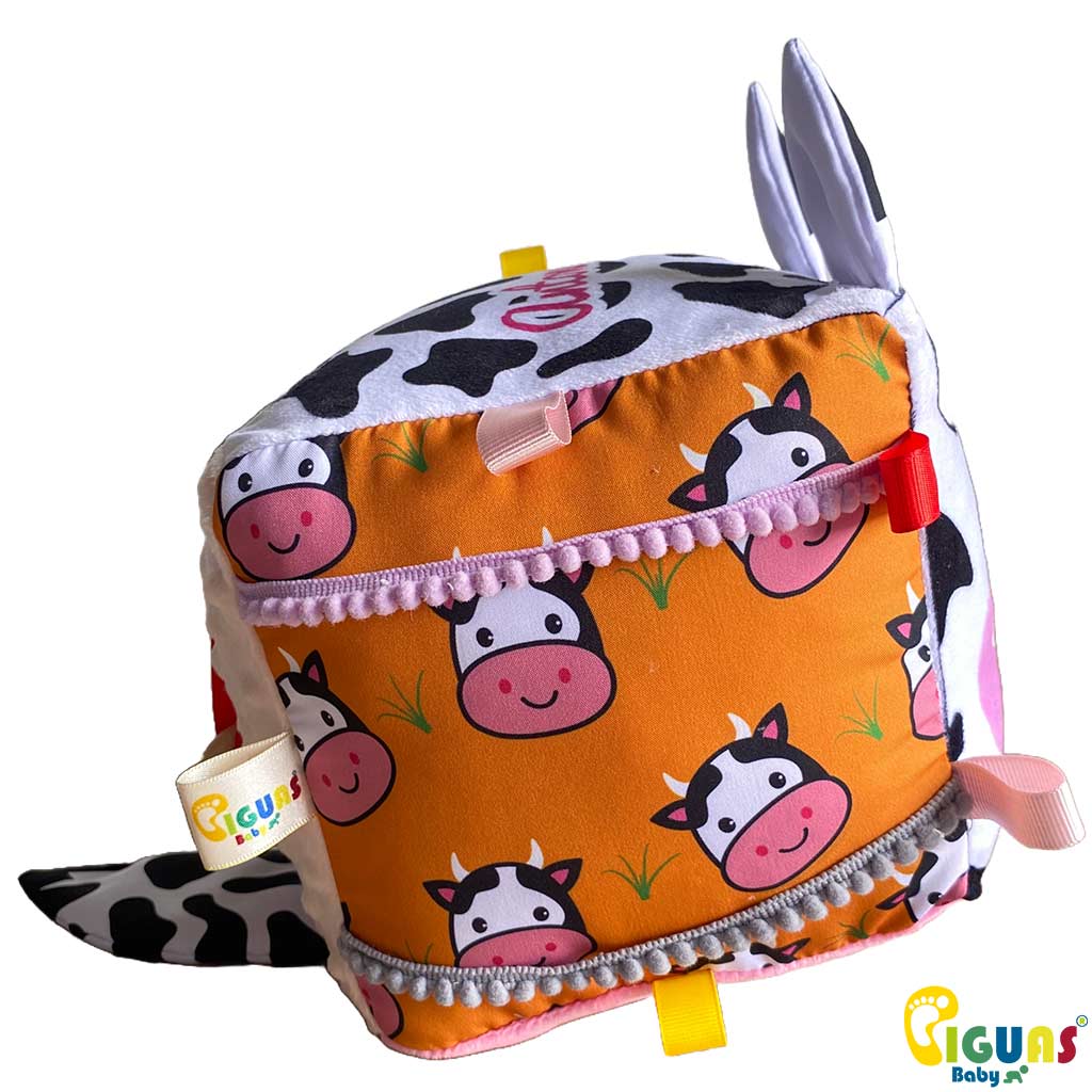 Un cubo sensorial para bebés con la cara de una vaca aventurera, perfecto para estimular la vista, la audición y el tacto de tu bebé.
