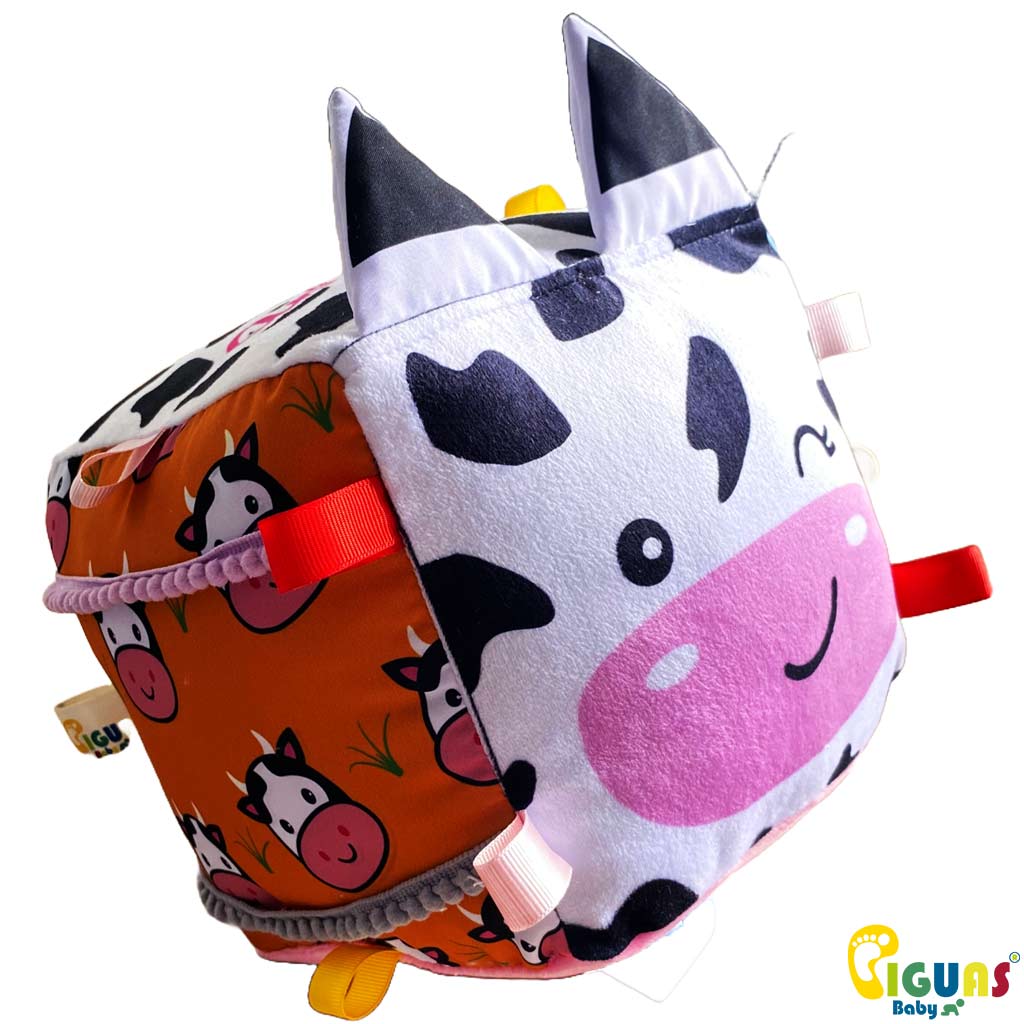 Un cubo sensorial para bebés con la cara de una vaca curiosa, con texturas suaves y llamativas, perfecto para estimular el tacto y la vista de tu pequeño